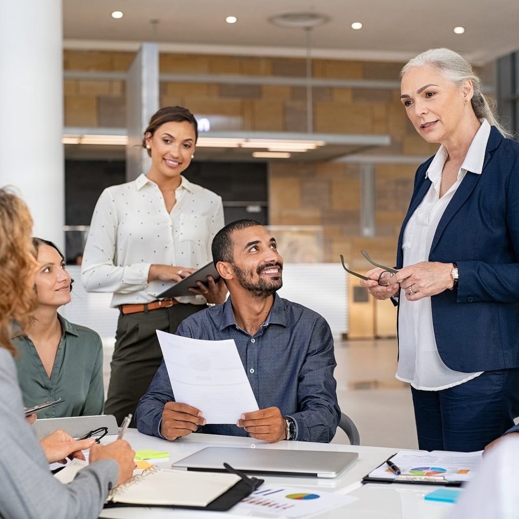Group of business people discussing work in conference room. Senior business manager guiding employees in meeting. Group of businessman and businesswoman working together while sharing new strategy.